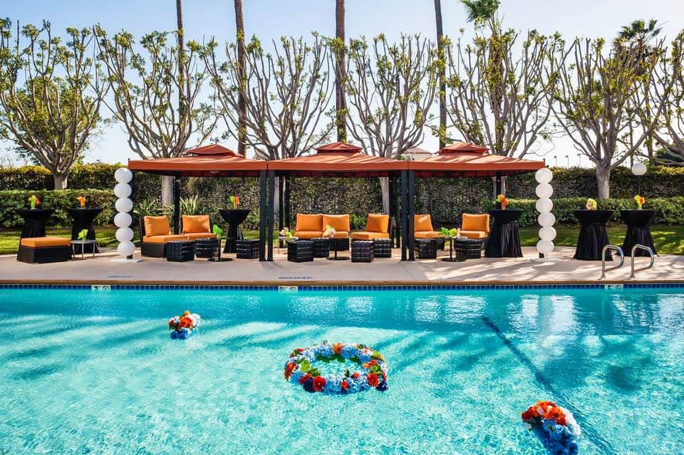 Poolside lounge area with orange seating under red umbrellas and decorative white pillars