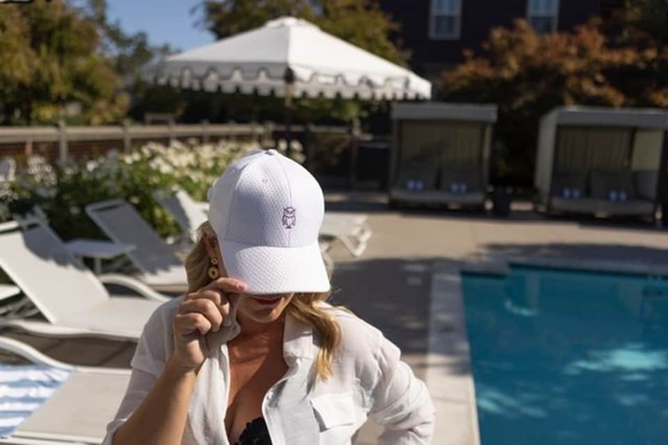 Woman in white cap at poolside with lounge chairs, white tent event space, and blue swimming pool in background