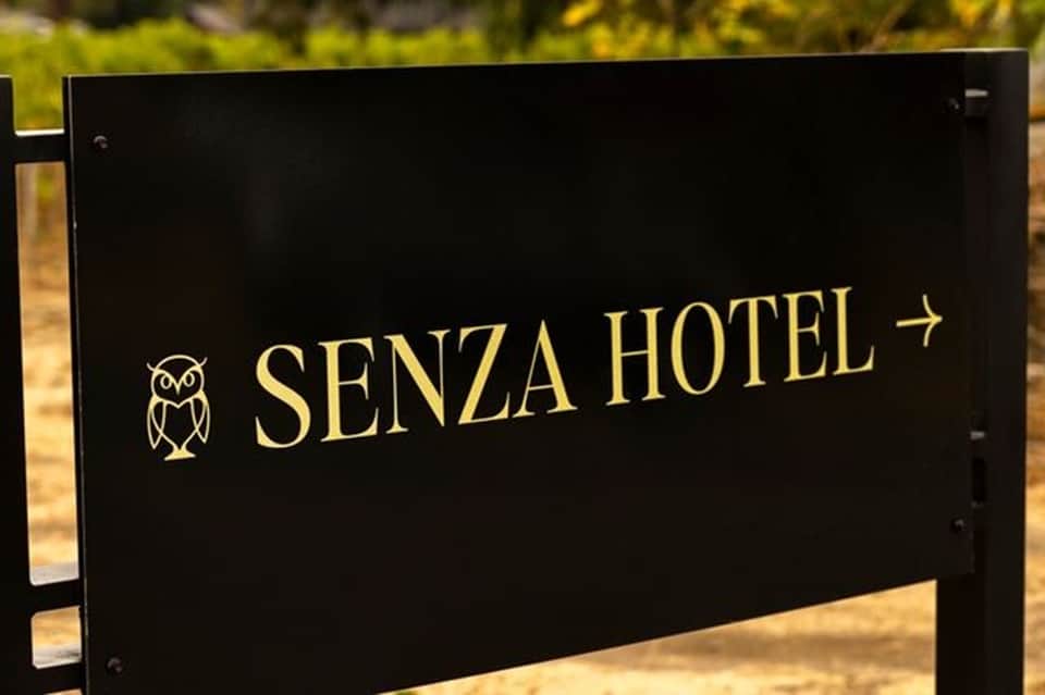 Senza Hotel directional sign with owl logo on black background nestled in nature setting