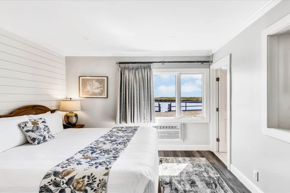 Coastal bedroom with white shiplap walls, queen bed, and waterfront balcony view