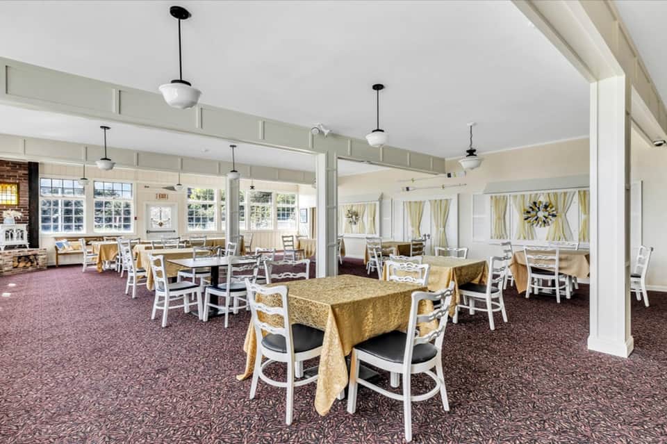 Bright dining room with white columns, tables with gold linens, pendant lighting, and large windows