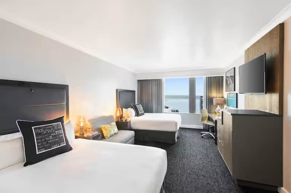 Upscale hotel bedroom with two beds, ocean view windows, modern furnishings, and flat-screen TV