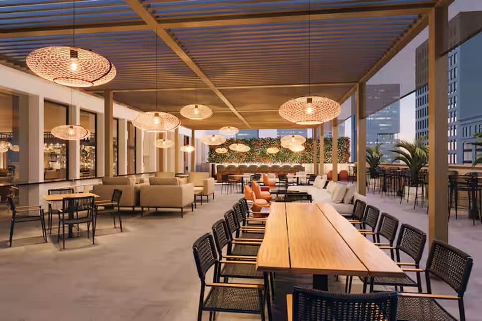 Modern rooftop terrace lounge with woven pendant lights, wooden long table, and urban cityscape in background