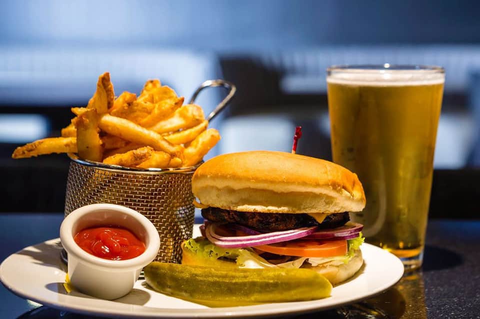 Gourmet burger with fries and beer on outdoor dining table with ocean view