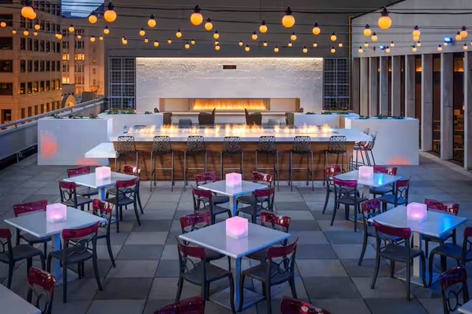 Rooftop bar and lounge with fireplace, hanging lights, glowing tables at night