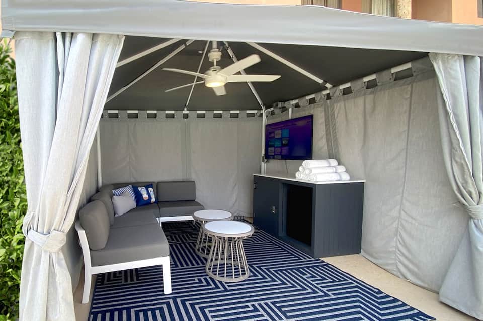 Covered patio lounge with gray seating, TV, ceiling fan, and decorative striped rug