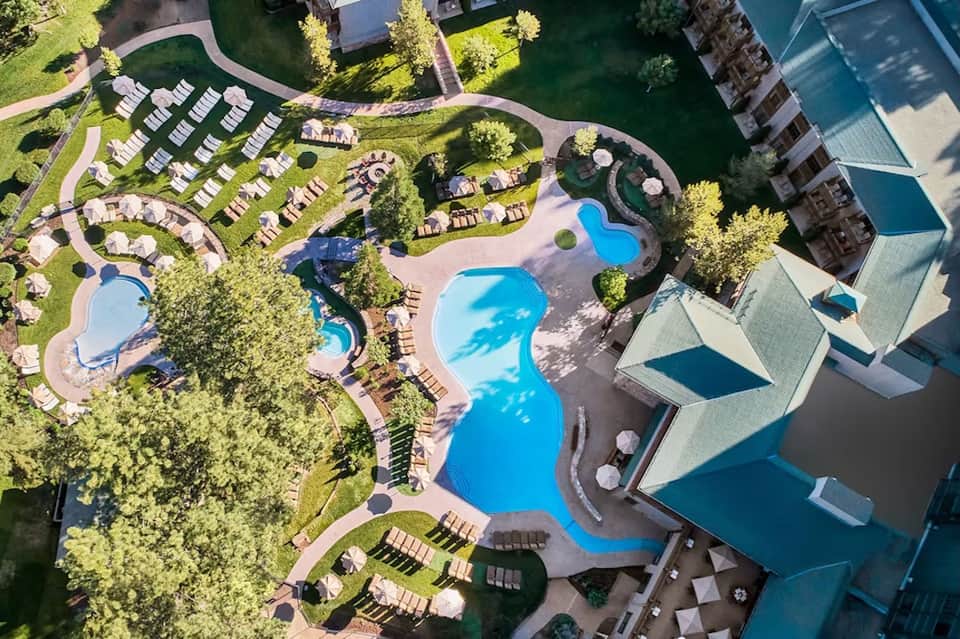 Aerial view of large resort with multiple shaped pools, landscaped grounds, and waterfront location