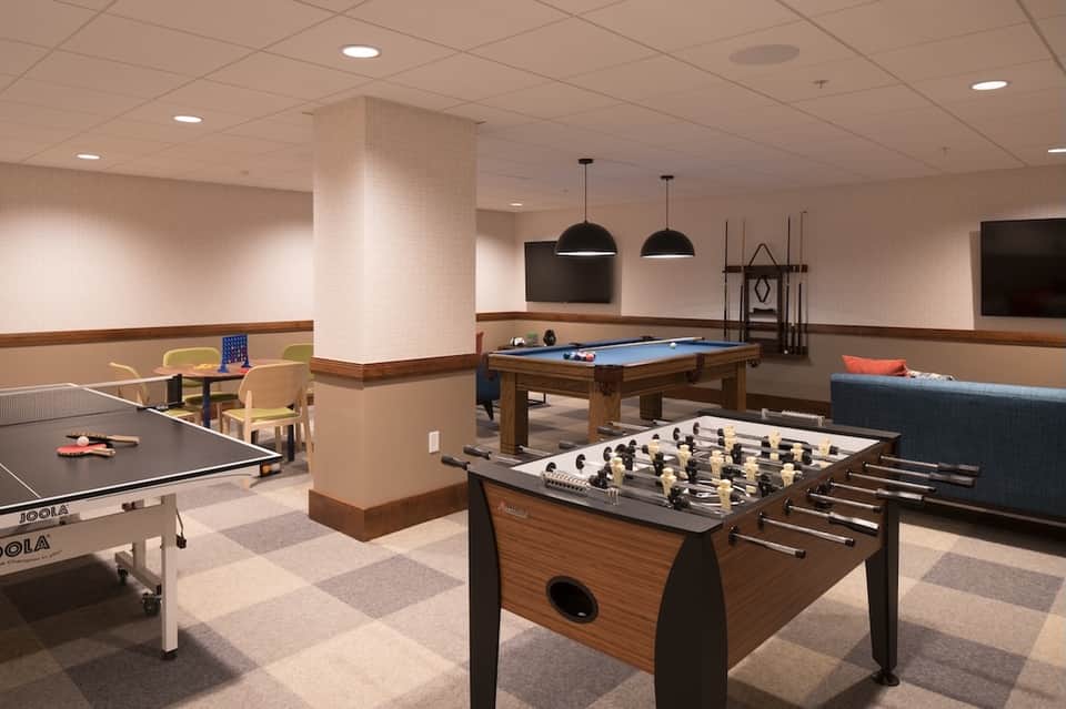 Games room with foosball table, billiards, ping pong, and lounge seating under pendant lights