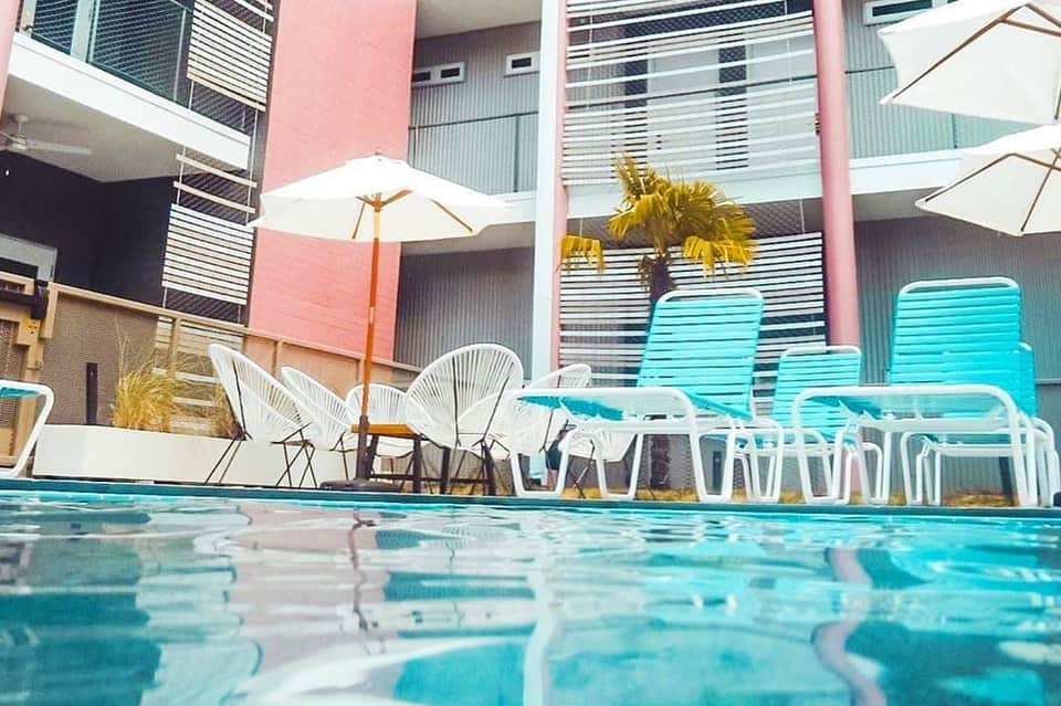Resort pool with turquoise loungers and white umbrellas, pink building facade in background