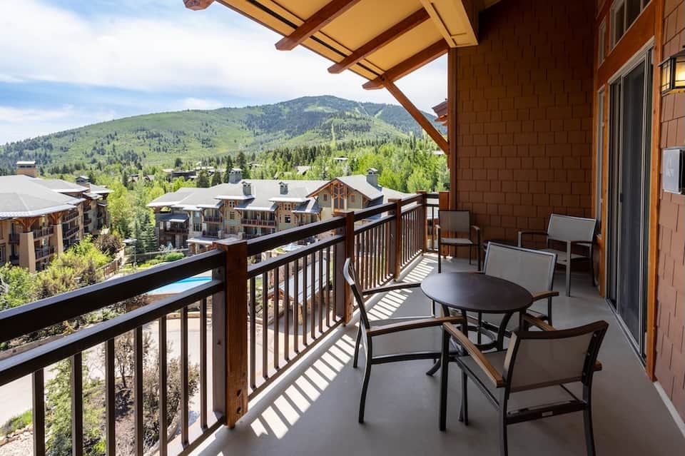 Mountain resort balcony with seating, dining table, and panoramic valley and ski slope views