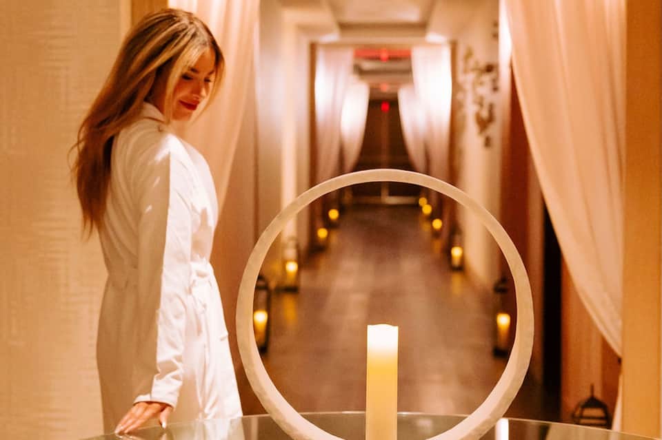 Woman in white spa robe walking down candlelit hallway with ambient golden lighting and elegant spa ambiance