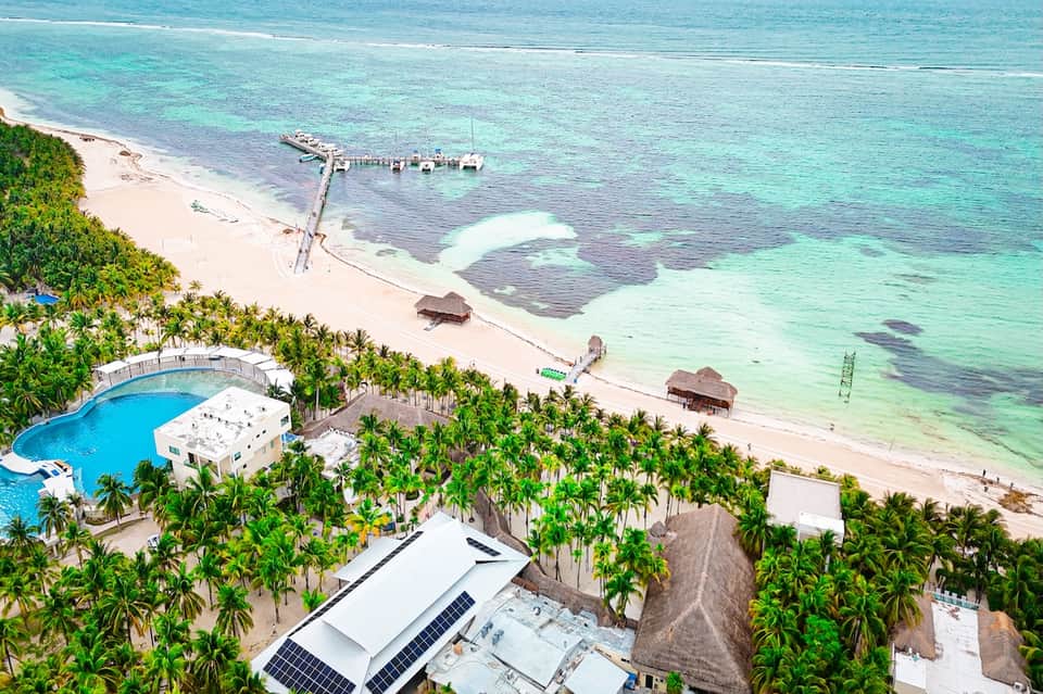 Aerial view of tropical beach resort with pool, palm trees, pier, and turquoise ocean