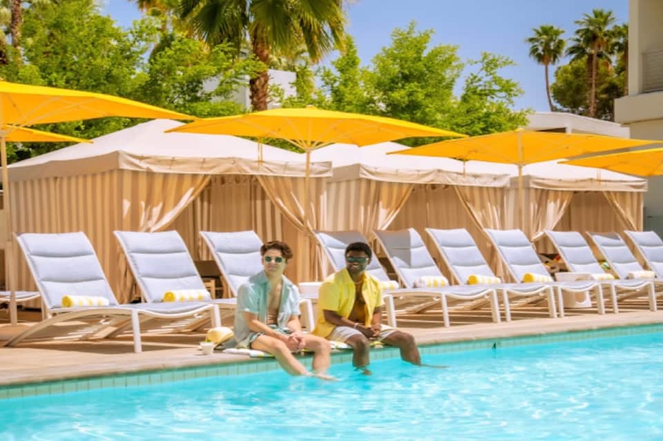 Resort pool deck with loungers, yellow umbrellas, and two guests sitting poolside