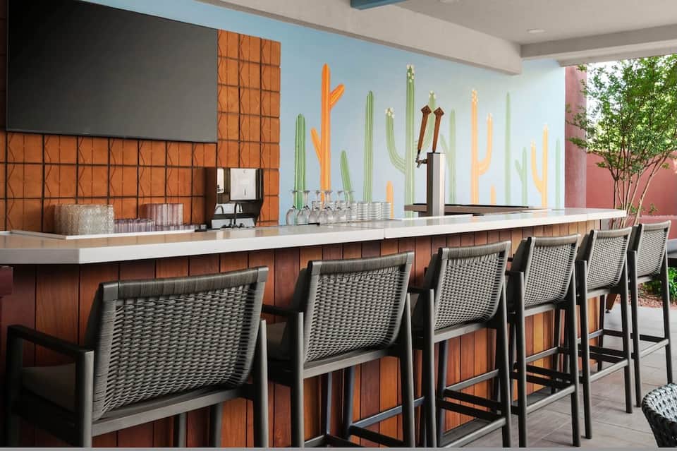 Modern bar counter with cactus wall mural, white countertop, mesh bar stools, and courtyard view