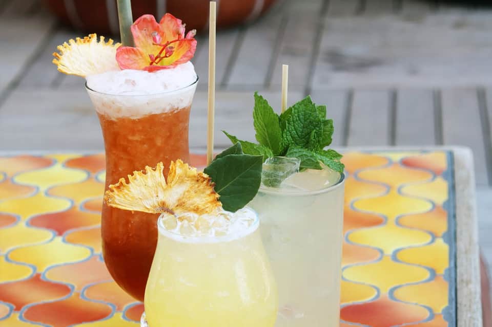 Three colorful tropical cocktails with floral garnishes on a patterned table