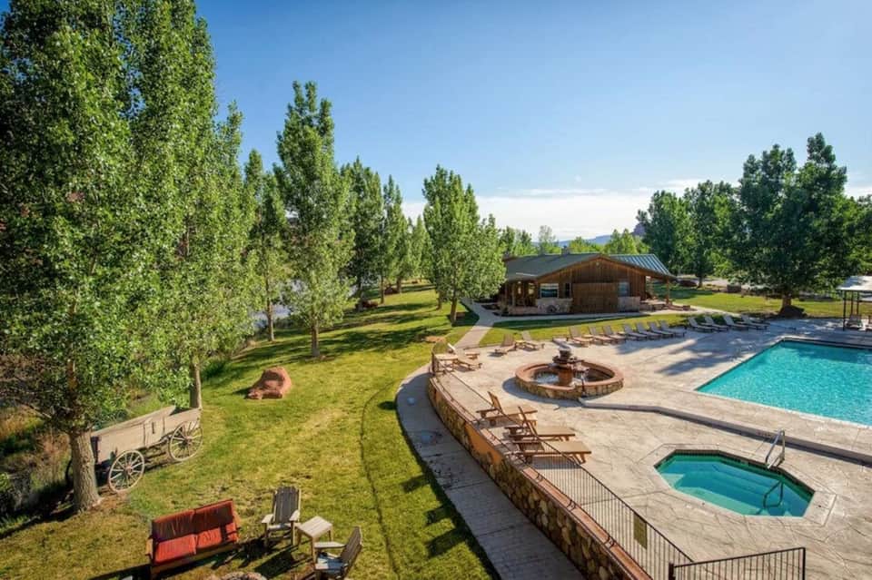 Scenic resort pool surrounded by tall trees, fire pit, spa building, and manicured green lawns