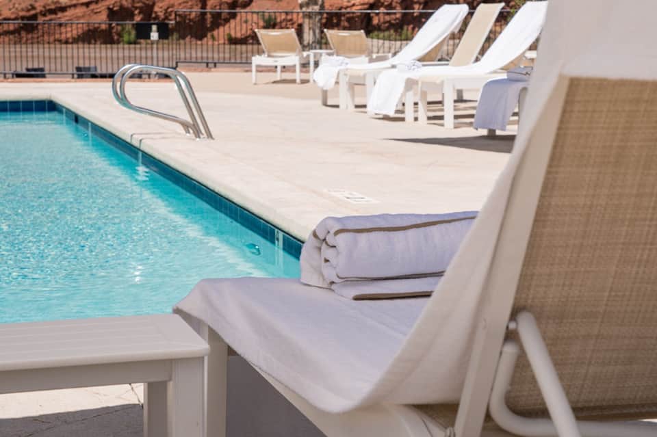 Pool deck with white lounge chairs, towels, clear turquoise water, and desert landscape backdrop