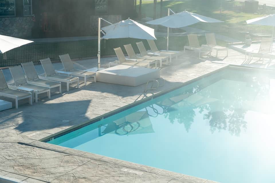 Resort pool area with turquoise water, white lounge chairs under umbrellas, and coastal buildings visible beyond