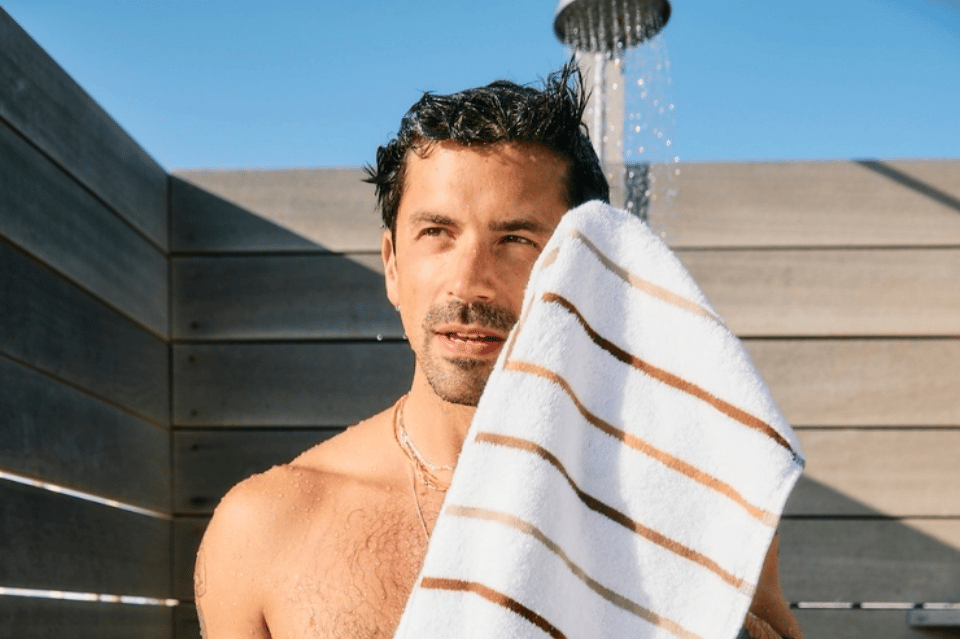 Man showering outdoors under rainfall showerhead with wet hair and towel