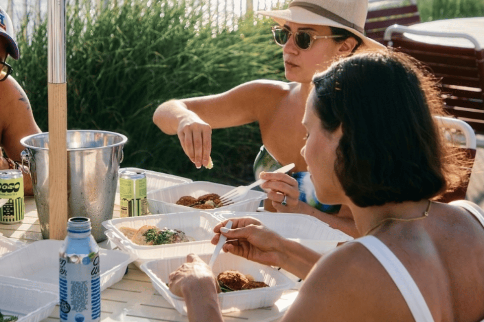 Guests enjoying casual lunch poolside with water pitcher and food on white patio furniture