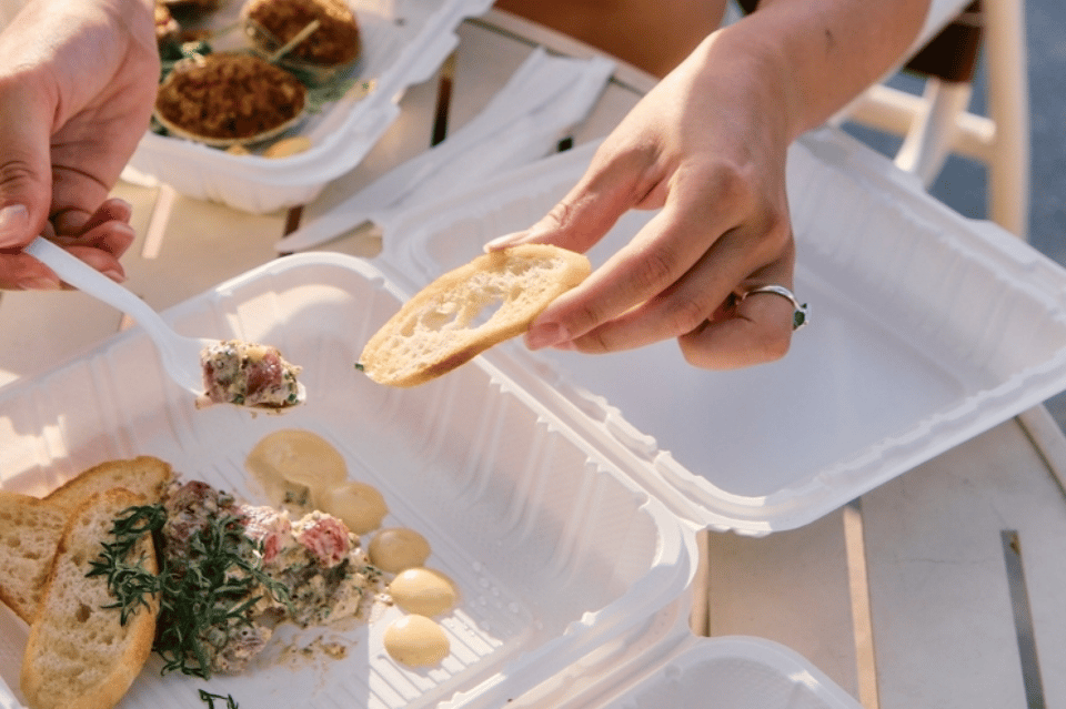 Hands holding food on white plate during beachside dining with appetizers