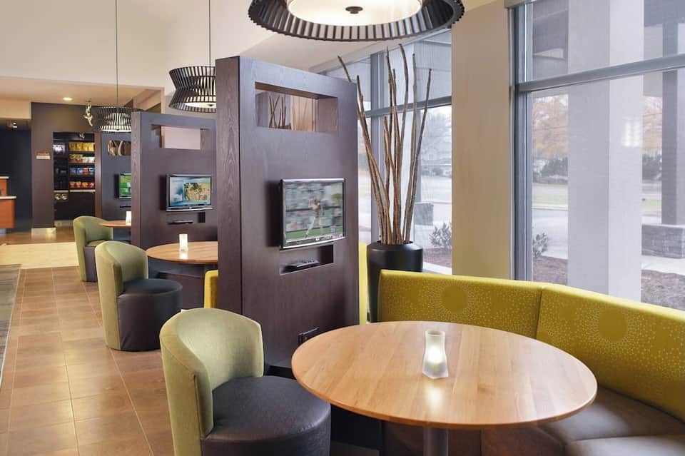 Modern hotel lobby lounge with contemporary furniture, decorative panels, TV screens, and large windows
