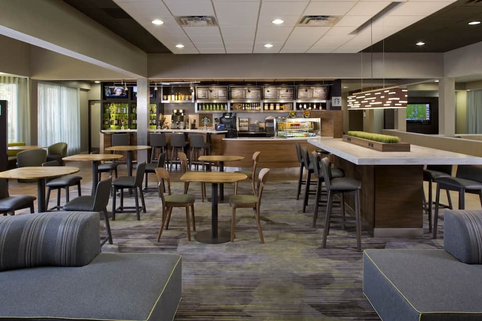 Contemporary hotel lobby and bar with wooden furniture, modern lighting, and casual seating