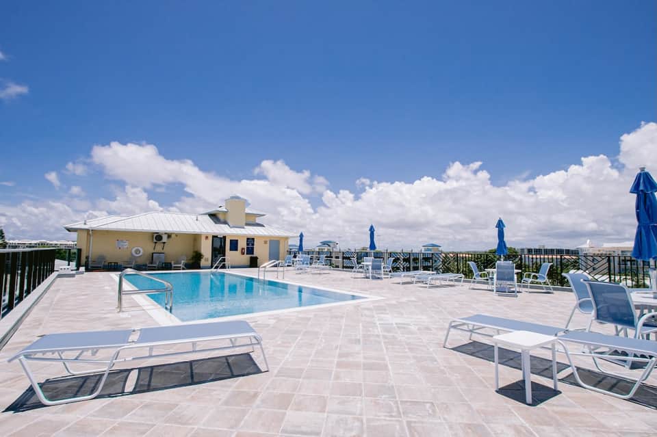 Rooftop pool deck with lounge chairs, umbrellas, and clear sky view