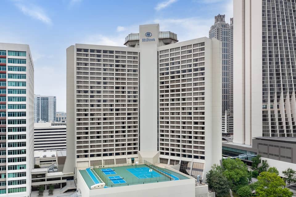 Tall Hilton hotel tower with multiple residential floors and rooftop tennis courts in urban skyline