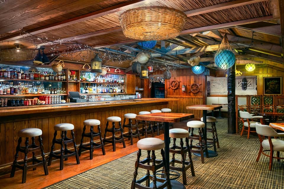 Rustic nautical bar interior with wooden beams, fishing nets, blue lanterns, and bar stools