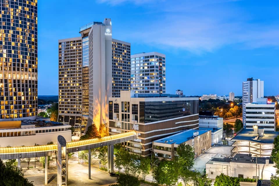Elevated urban hotel pool area at dusk with city skyline, illuminated buildings, and blue water
