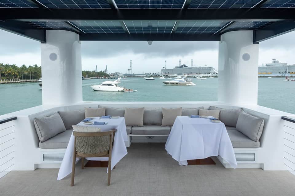 Luxury yacht dining area with gray seating, white tablecloths, and view of boats and marina