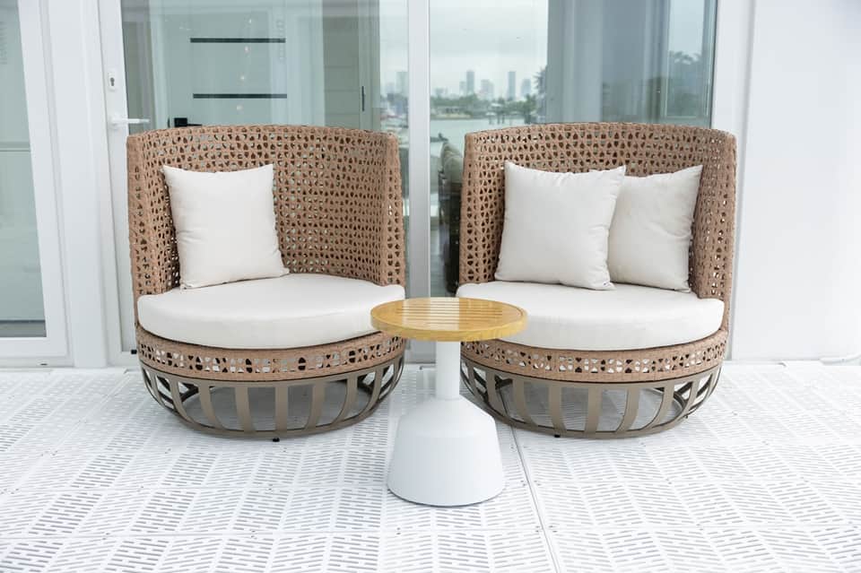 Coastal balcony with woven pod chairs, white cushions, and waterfront city skyline views
