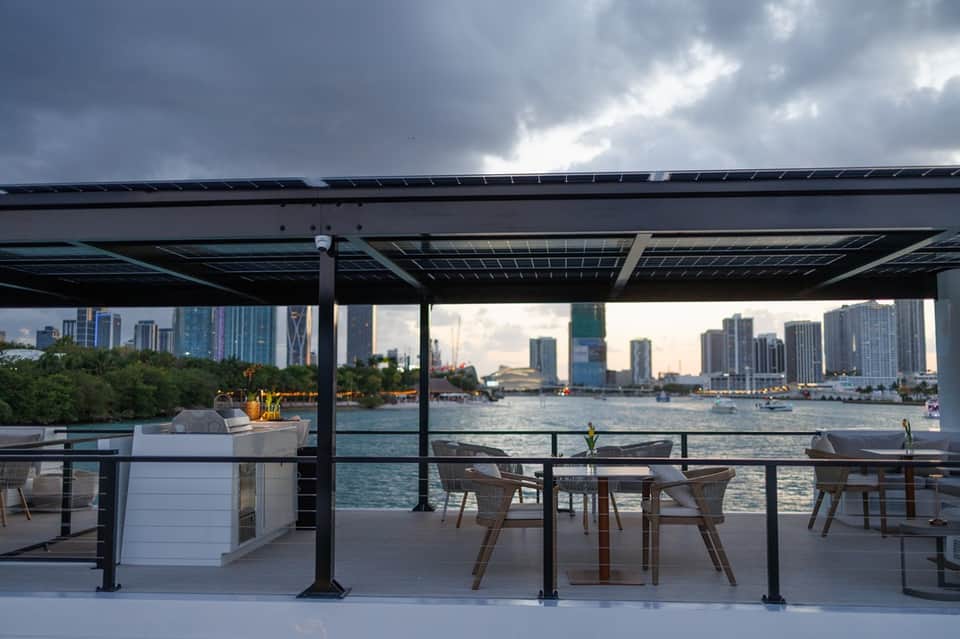 Waterfront rooftop terrace with dining tables, city skyline, and solar panels