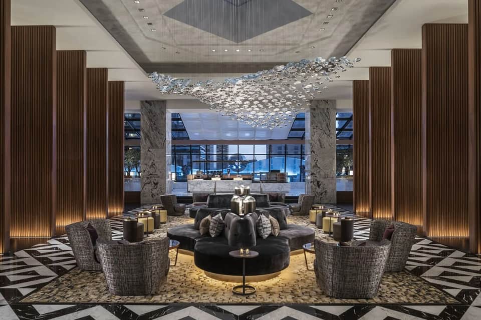 Upscale hotel lobby with chandelier, marble columns, seating areas, and floor-to-ceiling windows