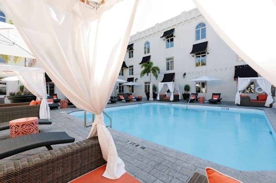 Courtyard pool with white draped cabanas, coral lounge chairs, and white building facade