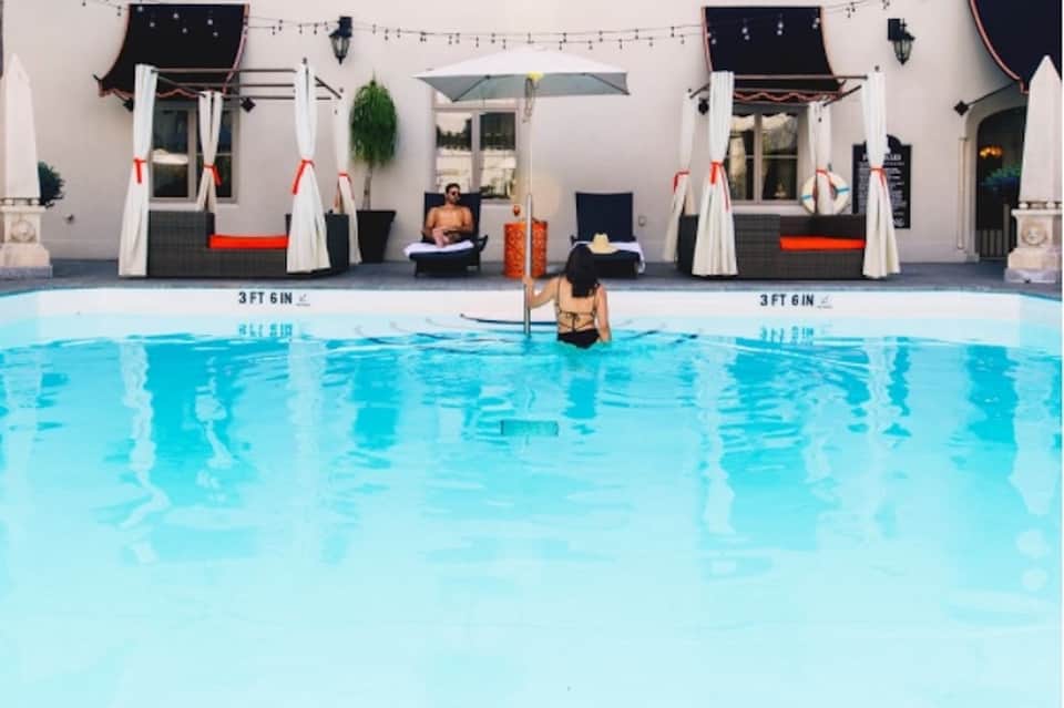 Resort pool with cabanas featuring white drapes, red accents, and poolside lounge seating