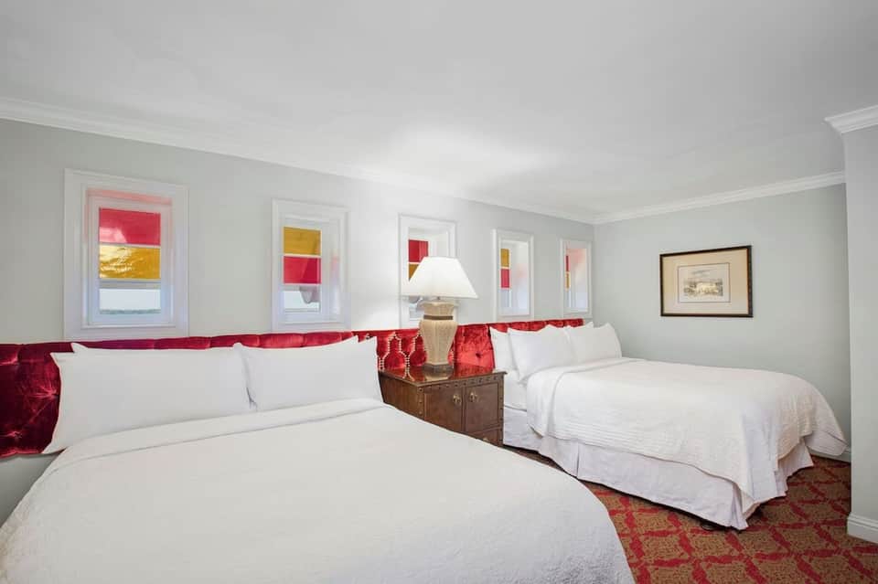 Hotel room with two queen beds, red accents, white linens, and ocean view windows