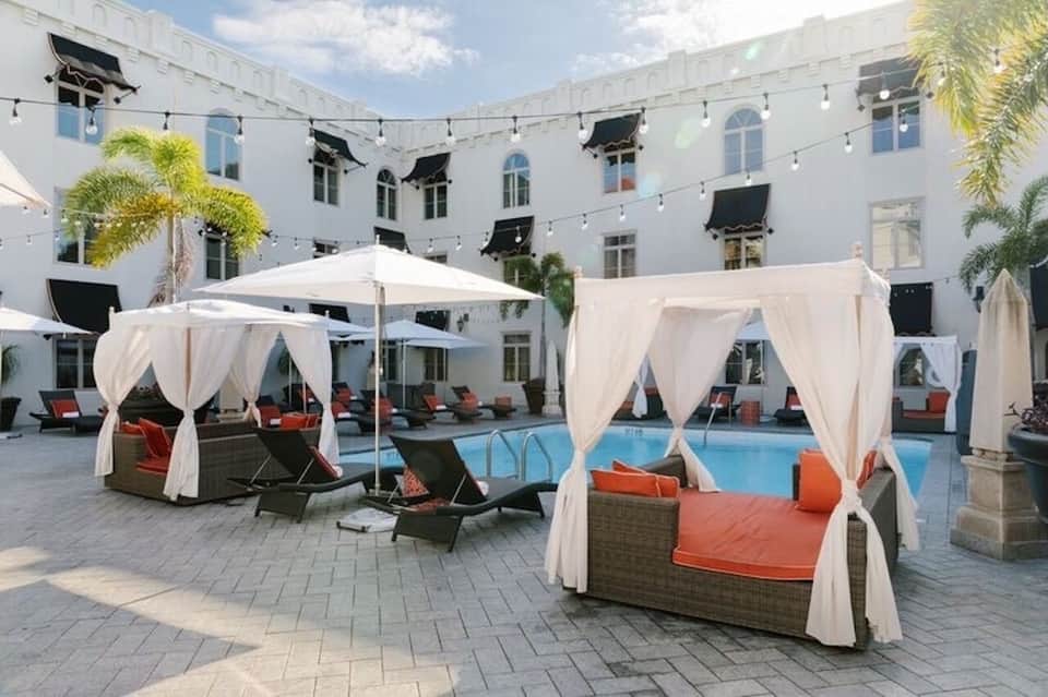 Courtyard pool surrounded by white cabanas with cream drapes, orange cushions, and palm trees