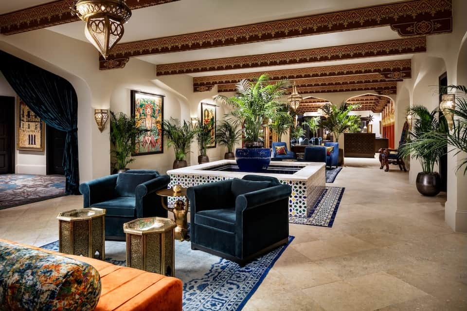 Grand hotel lobby with ornate beamed ceiling, blue velvet seating, and plants