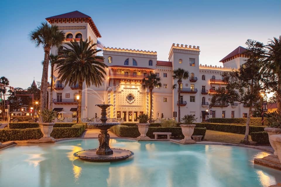Illuminated Spanish colonial-style resort building at dusk with palm trees and fountain courtyard