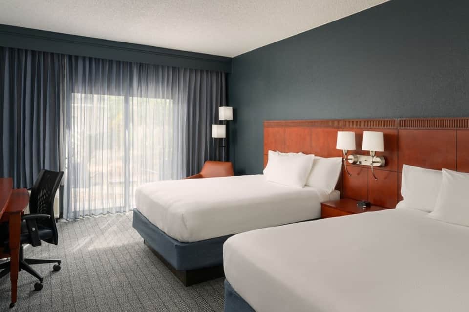 Hotel guest room with two queen beds, teal accent wall, and oceanview balcony doors