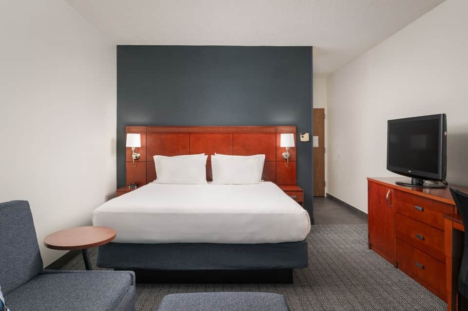 Hotel bedroom with orange headboard, white bedding, TV, and contemporary furnishings