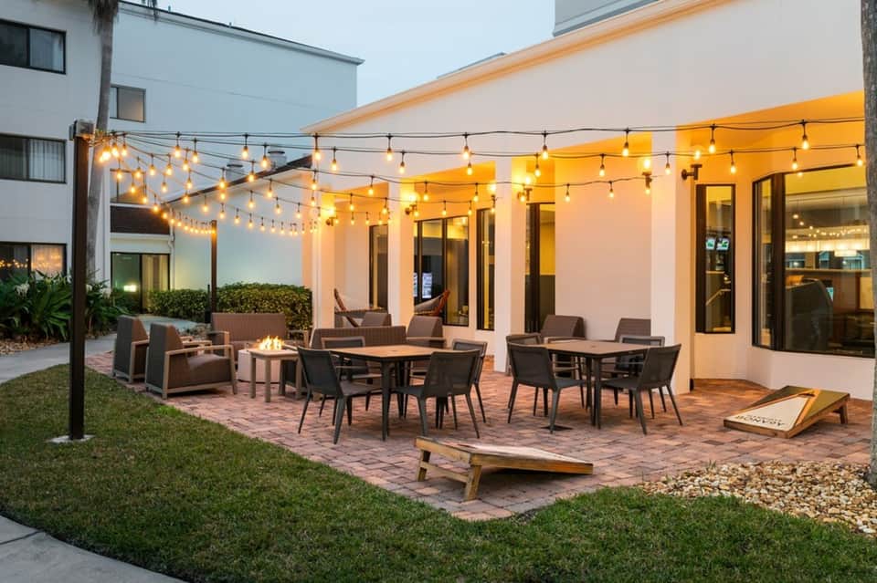 Outdoor patio with string lights, firepit, dining tables, and modern building at dusk