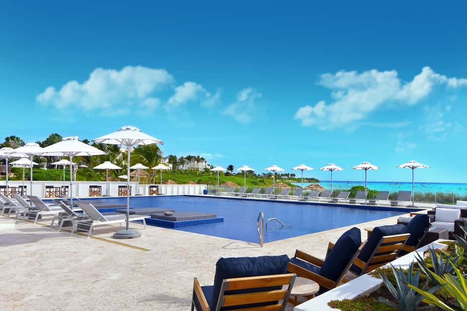 Oceanfront pool with white umbrellas, lounge chairs, and pristine turquoise water and beach