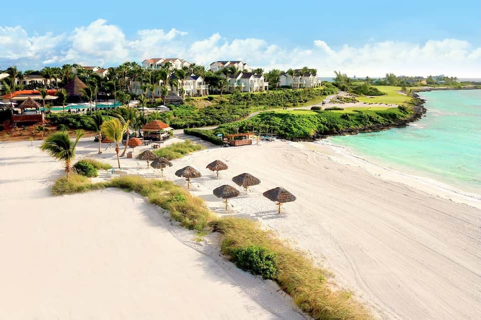 Beachfront resort with white buildings, palm trees, sand beach, and turquoise water