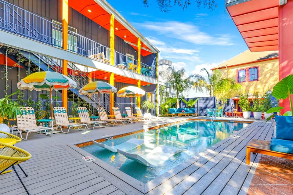 Vibrant resort pool area with colorful umbrellas, multi-story building, and tropical landscaping