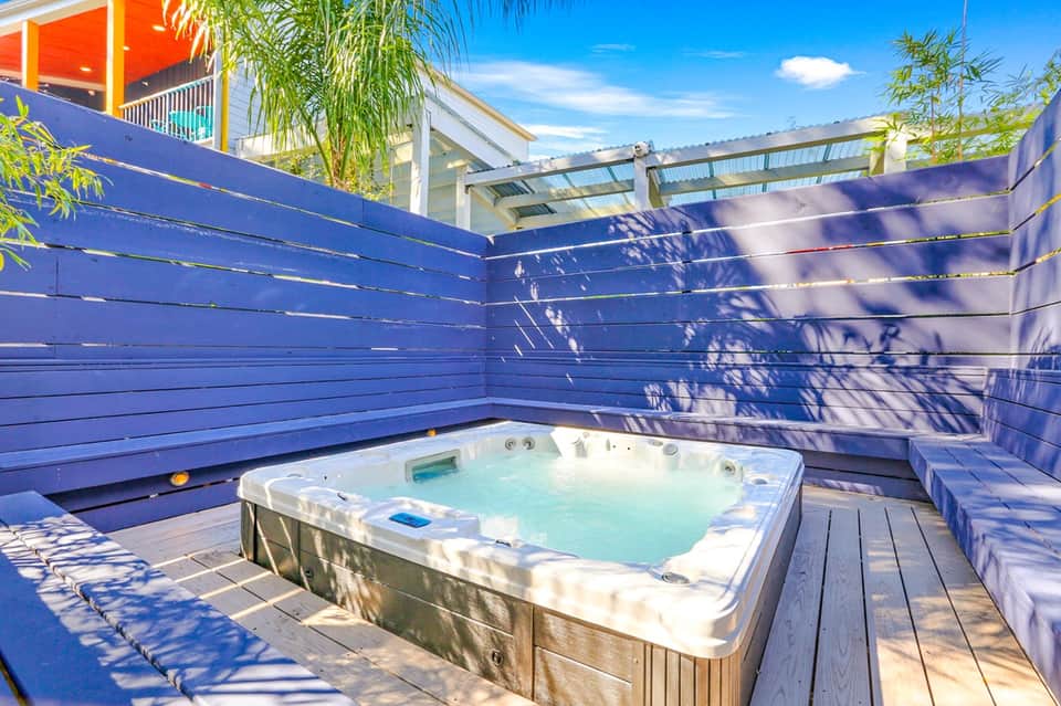 Modern hot tub on wooden deck enclosed by bright blue privacy panels with palm trees and contemporary architecture