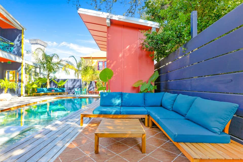 Vibrant poolside patio area with blue cushioned seating, wooden table, and colorful modern architecture