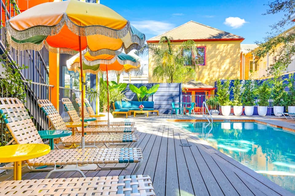 Colorful resort pool area with yellow umbrellas, lounge chairs, bright yellow building, and flowering planters